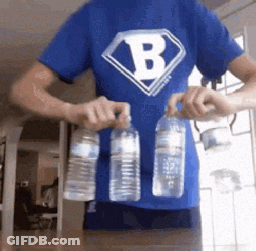 A Man Wearing A Blue Shirt With The Letter B On It Is Holding Two Water Bottles . GIF