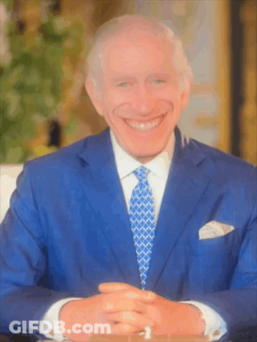 A Man Wearing A Blue Suit And Tie Smiles For The Camera GIF