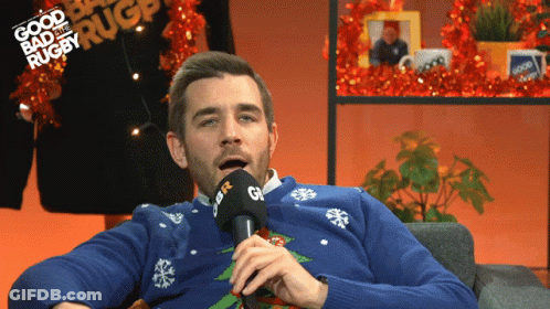 A Man Wearing A Blue Sweater Is Talking Into A Microphone With The Words Good Bad And Rugby Written In The Background GIF