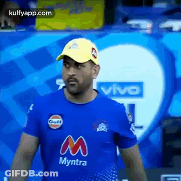 A Man Wearing A Blue T-Shirt And A Yellow Hat Is Standing In Front Of A Vivo Logo . GIF