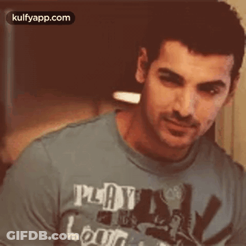 A Man Wearing A Blue T-Shirt That Says `` Play And Learn '' Is Looking At The Camera . GIF