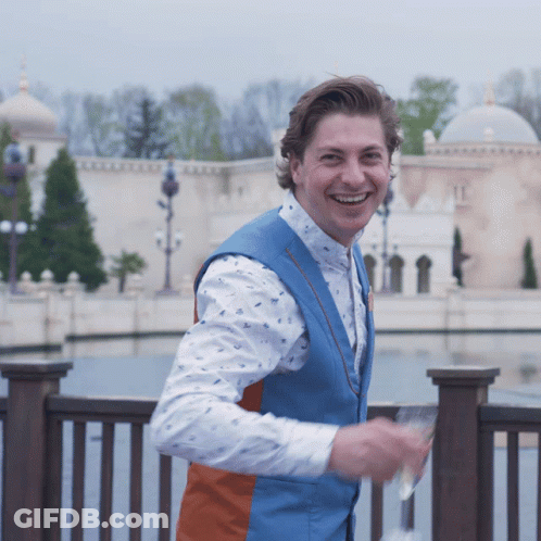 A Man Wearing A Blue Vest And A White Shirt Smiles GIF