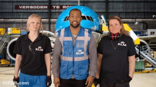 A Man Wearing A Blue Vest That Says Klm Stands Between Two Women GIF