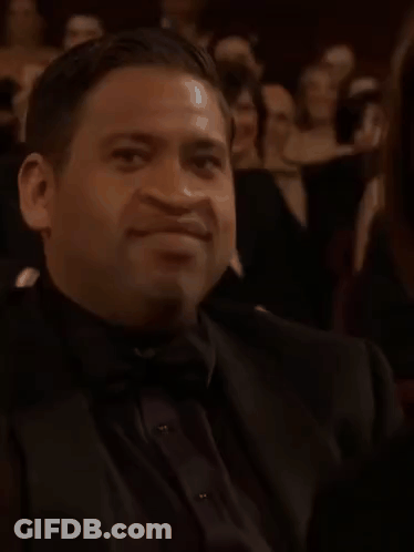 A Man Wearing A Bow Tie And A Ring Is Sitting In A Theatre . GIF