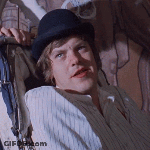 A Man Wearing A Bowler Hat And Striped Shirt Is Laying Down GIF