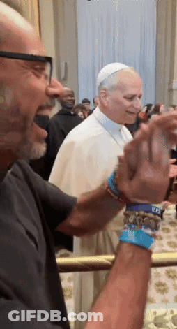 A Man Wearing A Bracelet That Says ' Dc ' On It Stands Next To A Man Wearing A White Hat GIF