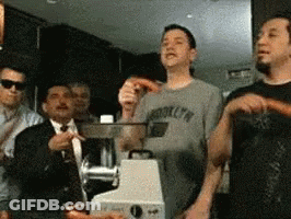 A Man Wearing A Brooklyn T-Shirt Stands In Front Of A Meat Grinder GIF