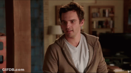 A Man Wearing A Brown Hoodie And A White Shirt Stands In A Living Room GIF