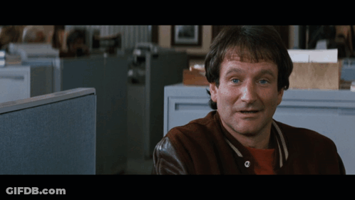 A Man Wearing A Brown Jacket Is Sitting In An Office Cubicle GIF