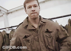 A Man Wearing A Brown Jacket Is Standing In Front Of A Rack Of Clothes GIF