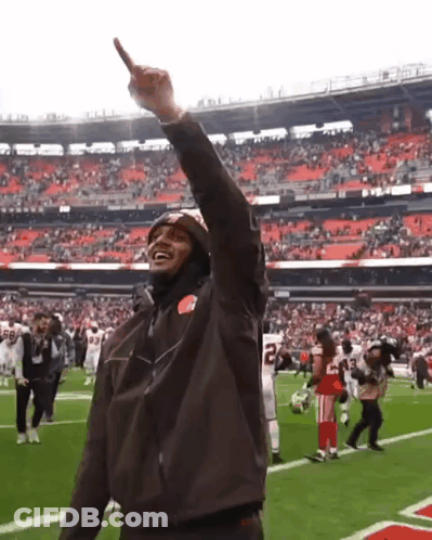 A Man Wearing A Brown Jacket With The Number 22 On It Stands On A Football Field GIF