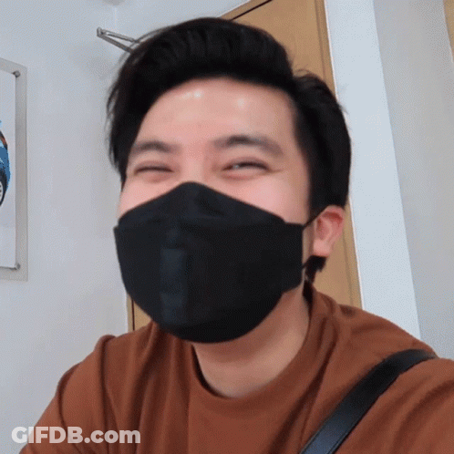 A Man Wearing A Brown Shirt And A Black Face Mask Smiles GIF