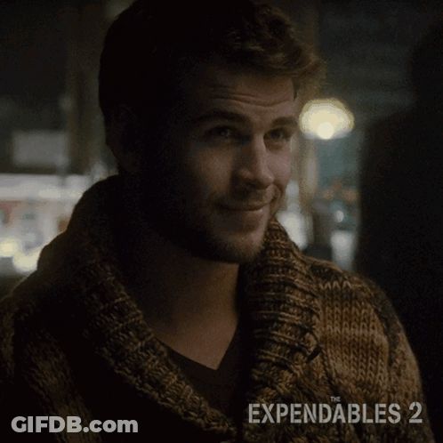 A Man Wearing A Brown Sweater With The Expendables 2 On The Bottom GIF