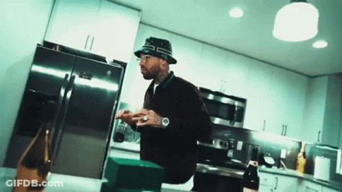A Man Wearing A Bucket Hat Is Standing In A Kitchen With A Bottle Of Champagne . GIF