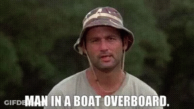 A Man Wearing A Bucket Hat Is Standing In Front Of A Green Background And Says `` Man In A Boat Overboard . '' GIF