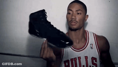A Man Wearing A Bulls Jersey Holds Up A Black Shoe GIF