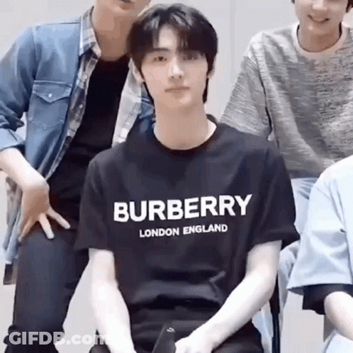 A Man Wearing A Burberry London England T-Shirt Is Sitting In Front Of A Group Of Men . GIF