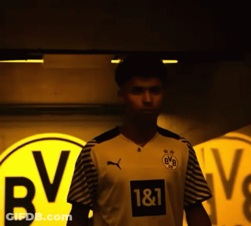 A Man Wearing A Bvb Jersey Stands In Front Of A Yellow Sign GIF
