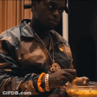 A Man Wearing A Camouflage Jacket Is Holding A Bowl Of Food . GIF