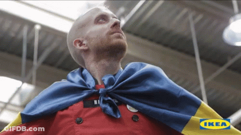 A Man Wearing A Cape With The Ikea Logo In The Corner GIF