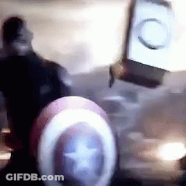 A Man Wearing A Captain America Shield Is Standing In A Dark Room . GIF