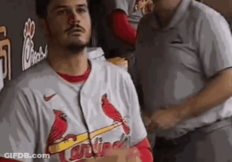 A Man Wearing A Cardinals Jersey Is Standing In A Dugout With A Red Nose . GIF