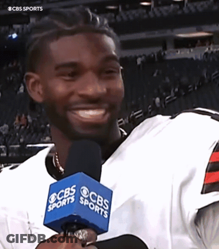 A Man Wearing A Cbs Sports Jersey Smiles While Holding A Microphone GIF