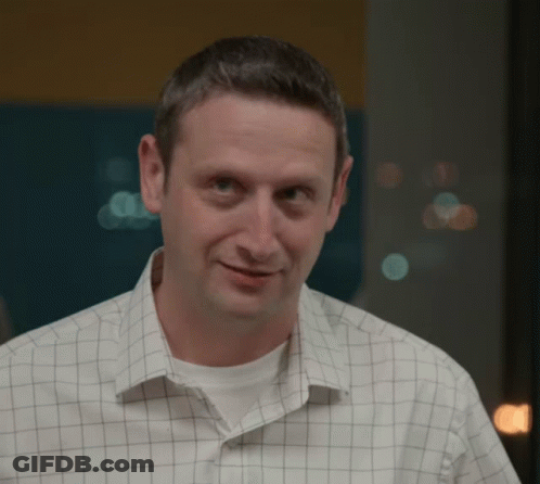 A Man Wearing A Checkered Shirt Looks At The Camera GIF