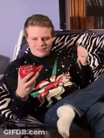 A Man Wearing A Christmas Sweater Holds A Red Heart GIF