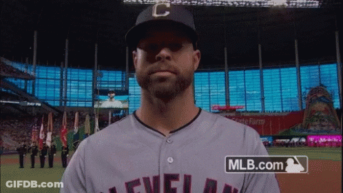 A Man Wearing A Cleveland Baseball Jersey Stands In Front Of A Mlb.com Logo GIF