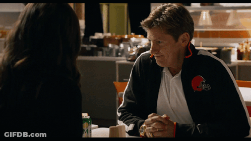 A Man Wearing A Cleveland Browns Jacket Is Talking To A Woman GIF