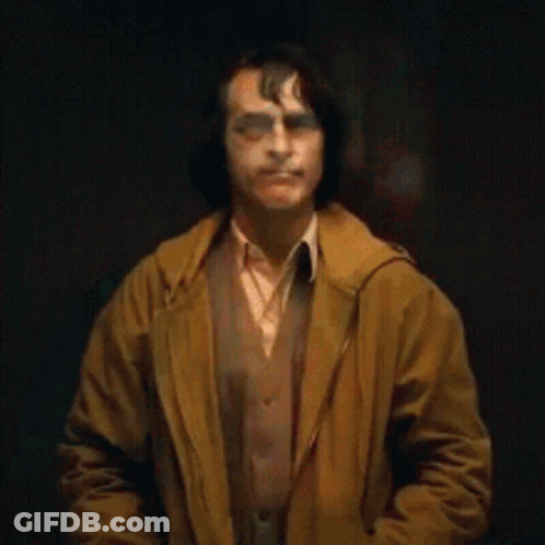 A Man Wearing A Clown Mask And A Brown Coat Is Smiling . GIF