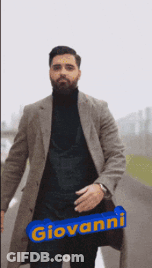 A Man Wearing A Coat And A Black Turtleneck Has The Name Giovanni Written On A Blue Sign GIF