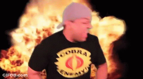 A Man Wearing A Cobra T-Shirt Stands In Front Of A Fire Explosion . GIF