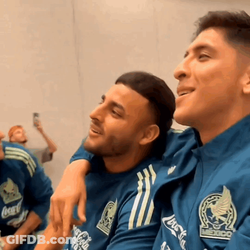 A Man Wearing A Coca Cola Shirt Sits Next To A Man Wearing A Mexico Shirt GIF