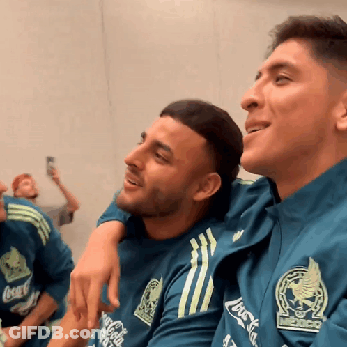 A Man Wearing A Coca Cola Shirt Sits Next To Another Man Wearing A Mexico Shirt GIF