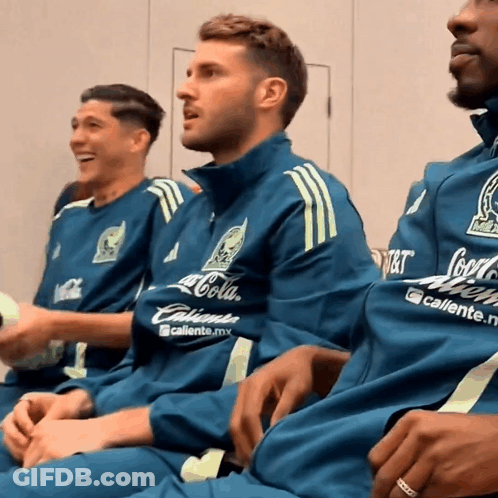 A Man Wearing A Coca Cola Shirt Sits With Two Other Men GIF