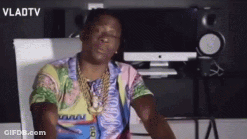 A Man Wearing A Colorful Shirt And A Gold Chain Is Sitting In Front Of A Computer . GIF