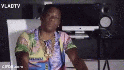 A Man Wearing A Colorful Shirt And A Gold Chain Is Sitting In Front Of A Computer . GIF