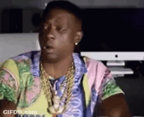 A Man Wearing A Colorful Shirt And A Necklace Is Sitting In Front Of A Computer . GIF