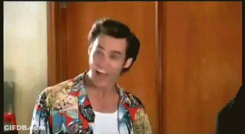 A Man Wearing A Colorful Shirt Is Standing In Front Of A Wooden Door . GIF