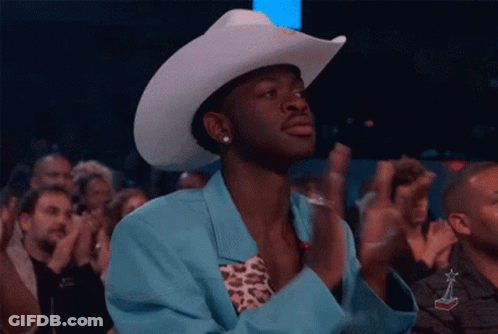 A Man Wearing A Cowboy Hat And A Blue Jacket Is Applauding In A Crowd . GIF