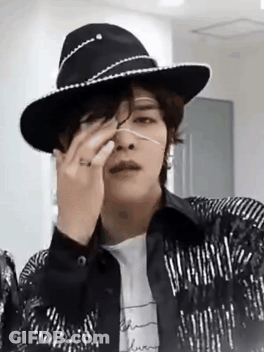 A Man Wearing A Cowboy Hat And A Jacket Is Covering His Nose With His Hand . GIF