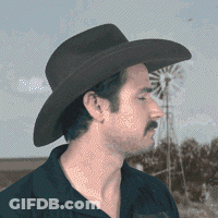 A Man Wearing A Cowboy Hat And A Mustache Stands In Front Of A Windmill GIF
