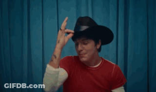 A Man Wearing A Cowboy Hat And A Red Shirt Is Smiling . GIF
