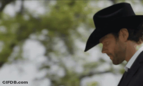 A Man Wearing A Cowboy Hat And A Suit Is Looking Down GIF