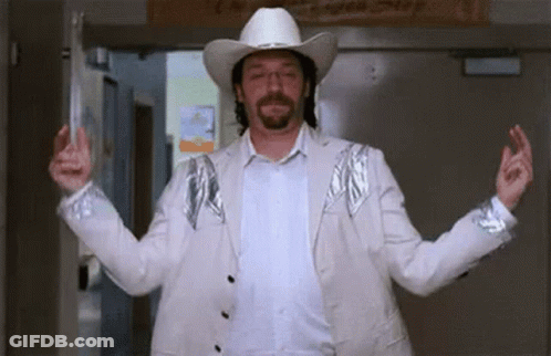 A Man Wearing A Cowboy Hat And A White Jacket Is Standing In A Hallway . GIF