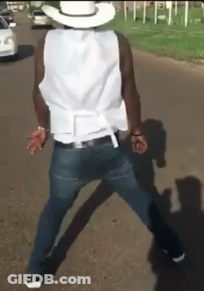 A Man Wearing A Cowboy Hat And A White Vest Is Walking Down The Street GIF