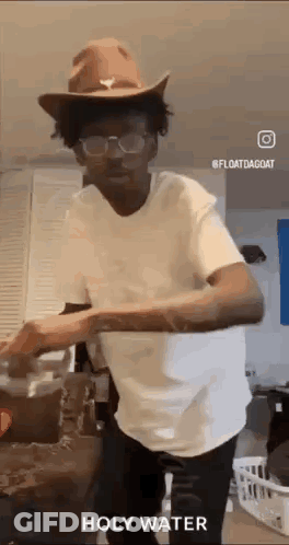 A Man Wearing A Cowboy Hat And Glasses Is Standing In A Kitchen . GIF