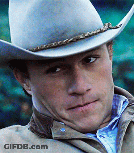 A Man Wearing A Cowboy Hat And Jacket Looks At The Camera GIF